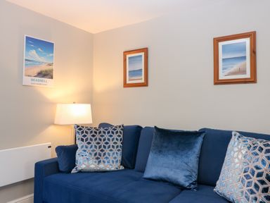 A living room with a blue sofa and pictures on the wall at Seaspray in Beadnell