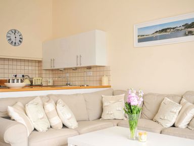 A living room with a sofa and kitchen area at 9 Slipway Cottages in Rock