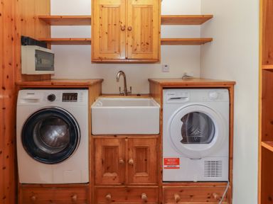 A laundry room with a washing machine, dryer, sink, and wooden cabinets at Ash House in Ballyvaughan