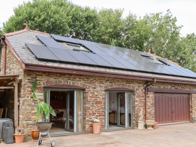 An outdoor area with a stone building and solar panels at Tigley Meadow Coach House in Totnes