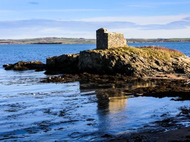A rocky outcrop with a building on top surrounded by water at Penrhos Walks in Holyhead