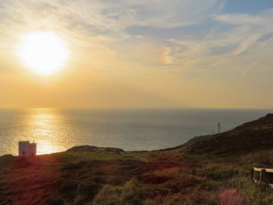 A seaside view with a sun setting over the ocean and a lighthouse at Penrhos Walks in Holyhead