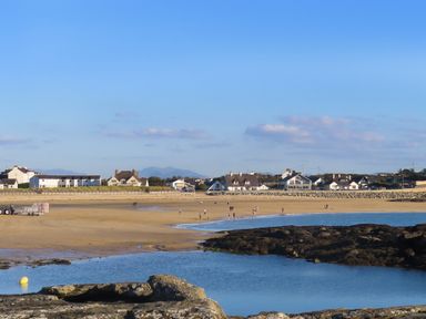 A beach with people walking near the water at Penrhos Walks in Holyhead