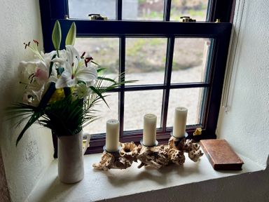 A window with flowers, candles, and a book at Cobble Stone Cottage near Leabgarrow, County Donegal