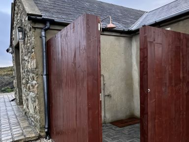 An outdoor shower area with wooden doors and a stone wall at Cobble Stone Cottage near Leabgarrow, County Donegal