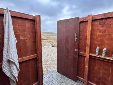 An outdoor shower area with a door open revealing bottles and a towel at Cobble Stone Cottage near Leabgarrow, County Donegal