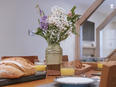 A dining room table with a flower vase juice and baked goods at Bluck's cottage in St. Agnes