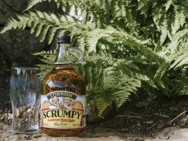 A bottle of Cornish Scrumpy cider and a glass next to ferns at Bluck's cottage St. Agnes