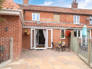 An outdoor patio with seating and a table at Honeysuckle Cottage in Swaffham