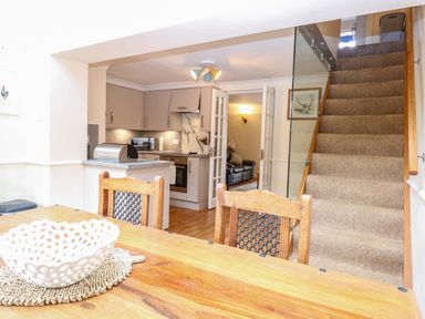 A dining room with a kitchen and staircase at Honeysuckle Cottage in Swaffham
