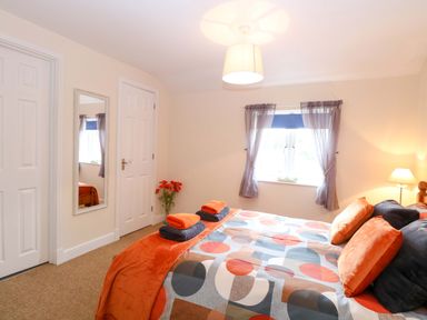 A bedroom with a bed, mirror, and window at Honeysuckle Cottage in Swaffham
