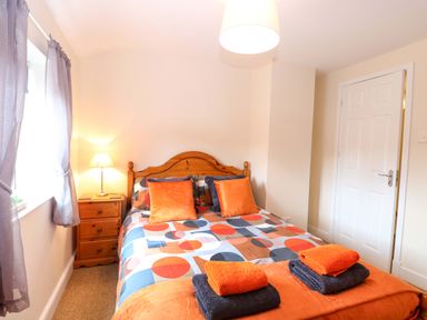 A bedroom with a bed and nightstand at Honeysuckle Cottage in Swaffham