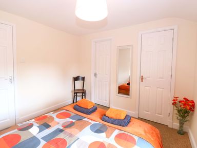 A bedroom with a bed, towels, chair, mirror and flower vase at Honeysuckle Cottage in Swaffham