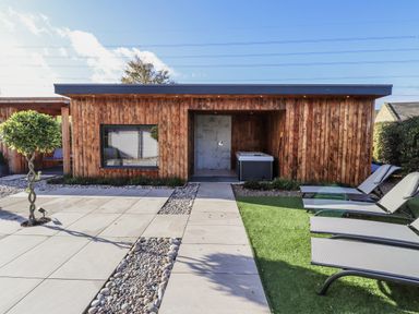 A wooden cabin with a hot tub and lounge chairs at Honeymug near Branton Powburn