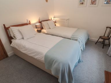 A bedroom with two beds and a chair at 1 Rowes Cottages in Penzance