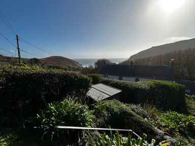 A view of the ocean and hills from a garden at 1 Rowes Cottages Porthgwarra