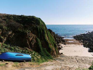 A view of a beach with a blue boat next to rocks at 1 Rowes Cottages in Porthgwarra