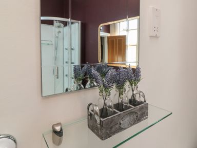 A bathroom with a mirror and flowers on a glass shelf at Stanton House - Abbey View, Flat 3