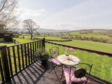 A deck with a table and chairs overlooking hills at Summertime Lodge in Rhyd-y-Foel near Abergele