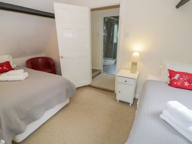 A bedroom with two beds and a door leading to a bathroom at Hillside Cottage