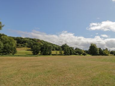 A field with trees and hills under a blue sky at Hillside Cottage in 