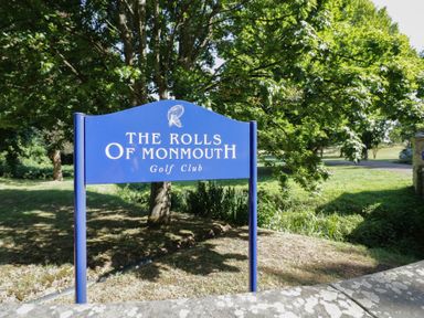 A sign for The Rolls of Monmouth Golf Club with trees and grass in the background