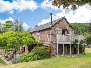 A brick and timber house with a wooden balcony and garden at The Cider Mill in Westhope near Leominster