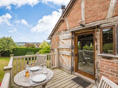 An outdoor wooden deck with a table set for two and wooden chairs next to a brick and timber house at The Cider Mill in Westhope near Leominster