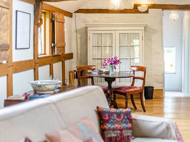 A dining area with a round wooden table and two chairs next to a white cabinet and a beige sofa in the foreground at The Cider Mill in Westhope near Leominster