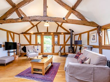 A living room with wooden beams a sofa armchair wood stove and coffee table at The Cider Mill in Westhope near Leominster
