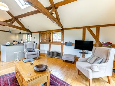 A living room with two armchairs a wooden coffee table a television and exposed wooden beams at The Cider Mill in Westhope near Leominster