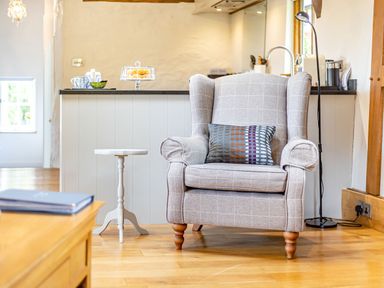An armchair with a patterned cushion next to a small round table in a room with wooden floors and a kitchen counter at The Cider Mill in Westhope near Leominster