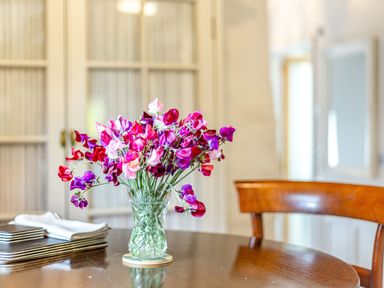 A glass vase with pink and purple flowers on a wooden dining table with a wooden chair in the background at The Cider Mill in Westhope near Leominster