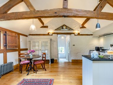 A kitchen and dining area with wooden beams and a round table with chairs at The Cider Mill in Westhope near Leominster
