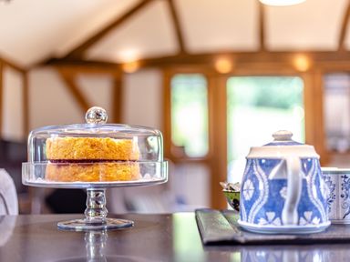 A cake on a glass cake stand and a blue and white teapot on a table in a room with wooden beams at The Cider Mill in Westhope near Leominster