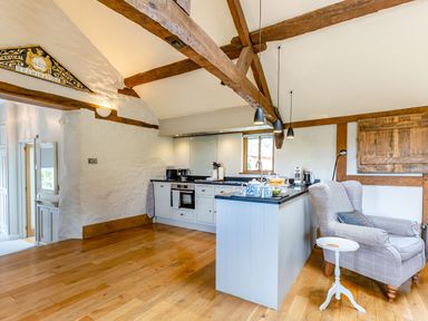 A kitchen with wooden beams white cabinets a grey armchair and a small white side table at The Cider Mill in Westhope near Leominster