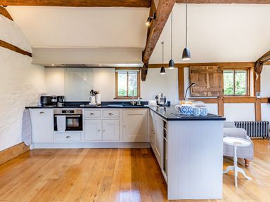 A kitchen with white cabinets black countertops wooden ceiling beams and wooden floor at The Cider Mill in Westhope near Leominster