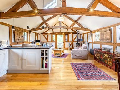 An open living space with wooden beams a kitchen island sofas rugs and a decorated chest at The Cider Mill in Westhope near Leominster