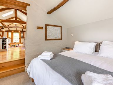 A bedroom with a bed folded towels and a map on the wall next to a living area with wooden beams at The Cider Mill in Westhope near Leominster