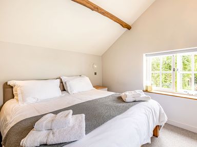 A bedroom with a double bed white linens folded towels bedside table and a window showing greenery at The Cider Mill in Westhope near Leominster