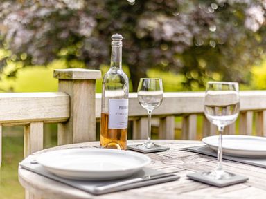 A wooden outdoor table set with two plates two wine glasses and a bottle of wine at The Cider Mill in Westhope near Leominster