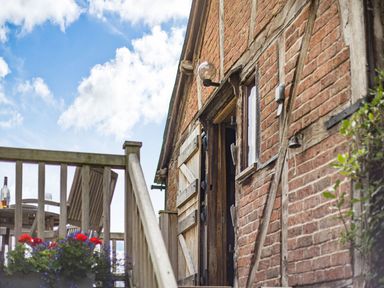 An outdoor wooden staircase leading to a patio with a table and chairs next to a brick building with a wooden door and window at The Cider Mill in Westhope near Leominster