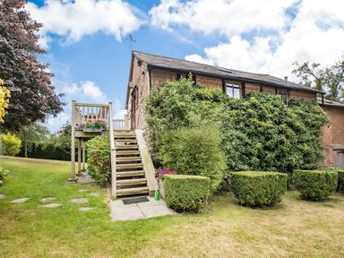 A garden with a wooden staircase and trimmed bushes beside a brick house covered in ivy at The Cider Mill in Westhope near Leominster