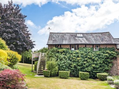 A garden with trimmed bushes and a wooden staircase next to a vine-covered brick house at The Cider Mill in Westhope near Leominster