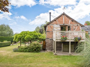 A garden with grass lawn and pergola next to a brick and timber house with a balcony at The Cider Mill in Westhope near Leominster