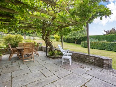 A patio with wooden chairs and table under a pergola with greenery at The Cider Mill in Westhope near Leominster