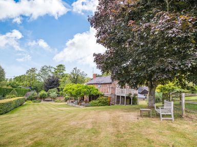 A garden with a large tree a wooden bench and table and a house surrounded by plants at The Cider Mill in Westhope near Leominster