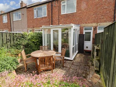 A garden with a conservatory and a table with chairs at Rose Briar Cottage Morpeth