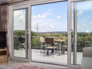 A patio with a table and chairs overlooking the countryside at Maple Lodge in Teigngrace near Kingsteignton