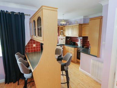 A kitchen with bar stools and cabinets at Kathleens Cosy Apartment in Galway